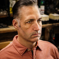After shot of a man in a barbershop with dark hair slicked back in a clean side-parted style using Imperial Blacktop Pomade.